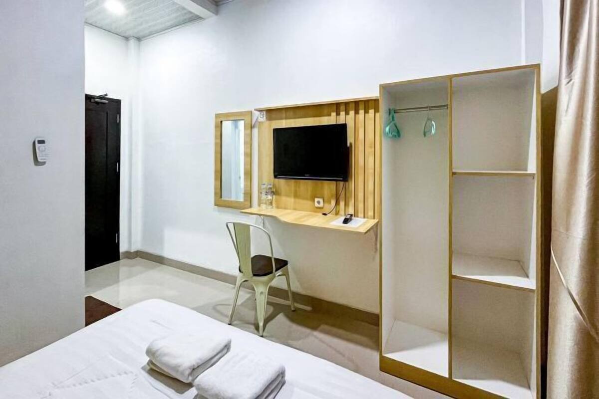 A hotel room with a bed, a desk with a computer, a chair, a TV, and a wardrobe.