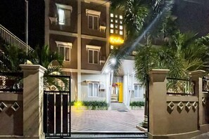 A multi-story building with a gated entrance, a well-lit pathway, and a small garden area with plants. - RedDoorz Plus @ Krishna Homestay Kupang (Kupang)