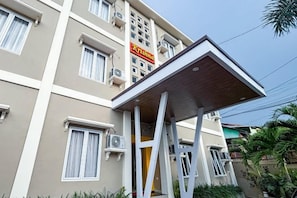 A multi-story hotel with a flat facade, air conditioning units, and a sign indicating the name. - RedDoorz Plus @ Krishna Homestay Kupang (Kupang)