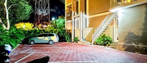 A paved driveway leading to a building with a staircase and a parked car.