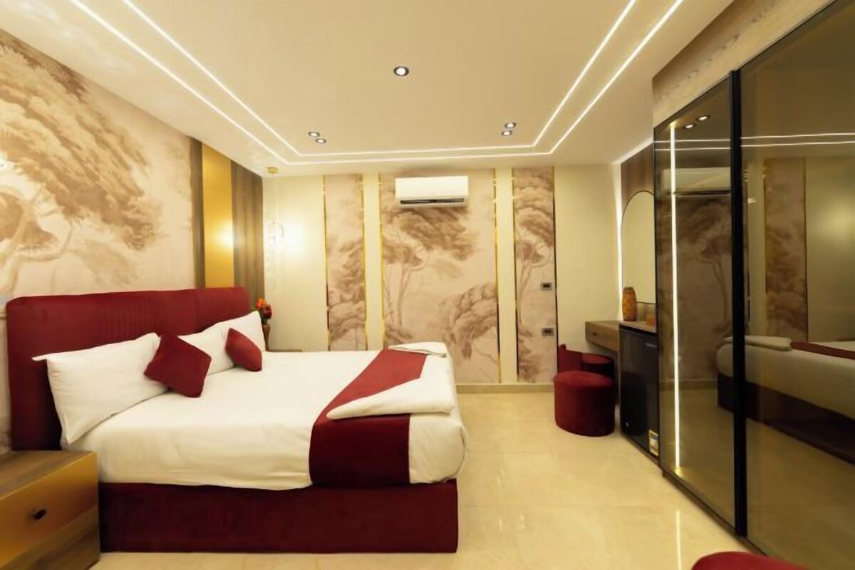 A modern bedroom with a large bed, a desk, and a glass partition.