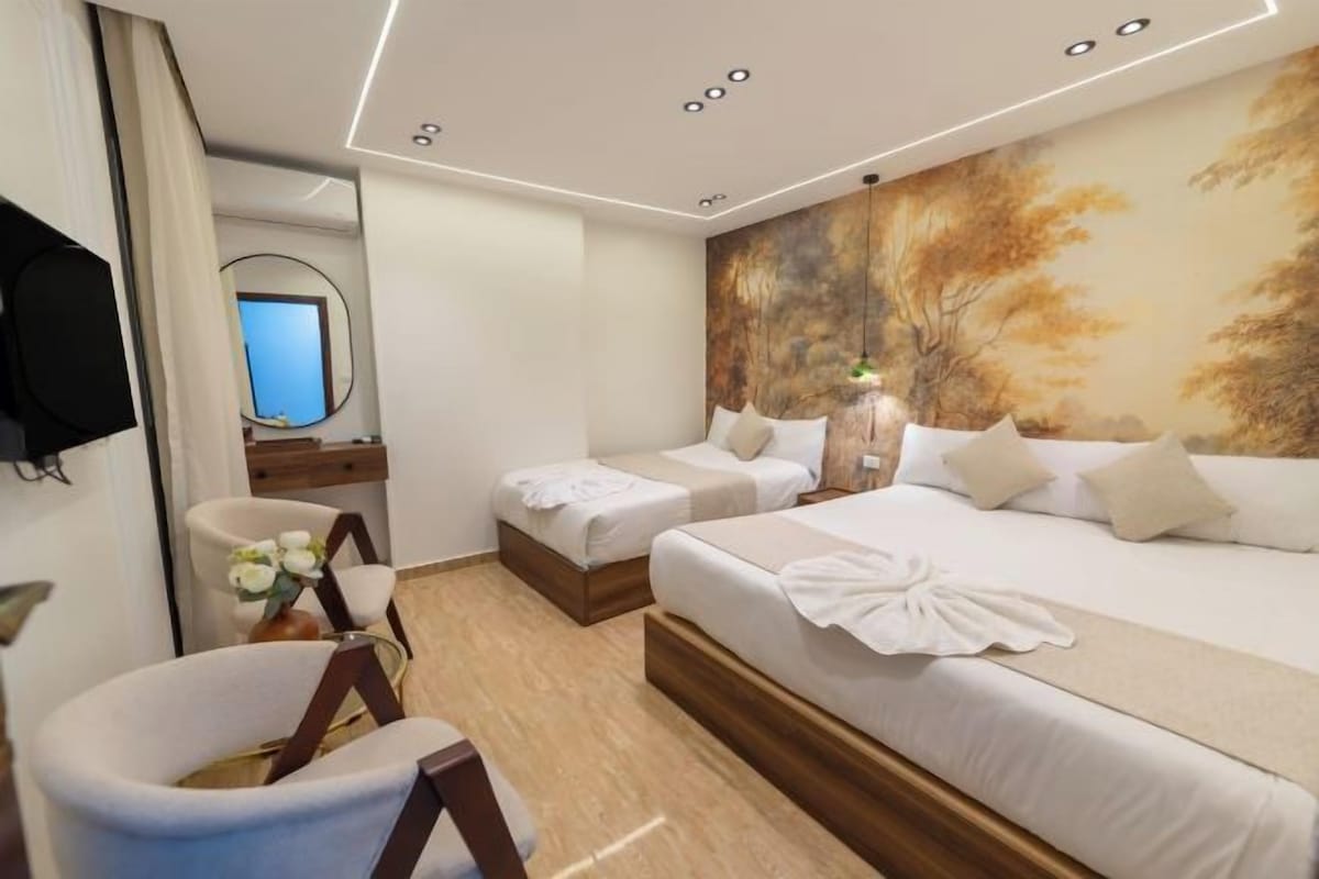 A hotel room with two beds, a desk, a chair, and a large painting on the wall.