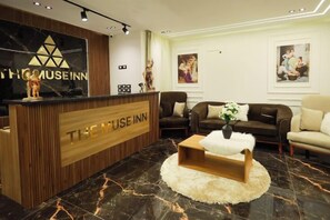 Una recepción con mostrador de madera y un logo, una zona de estar con sofás de cuero y un piso de mármol.