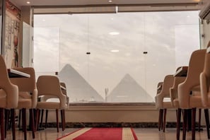 A room with a red carpet, a large window, and a view of pyramids. - The Muse Pyramids INN (Kafr Nassar)