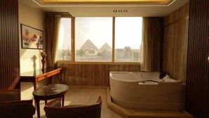 A room with a large window, a bathtub, a small table, and a chair. - The Muse Pyramids INN (Kafr Nassar)