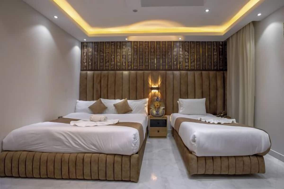 Una habitació d'hotel amb dos llits, un panell decoratiu a la paret i una tauleta de nit amb una làmpada.