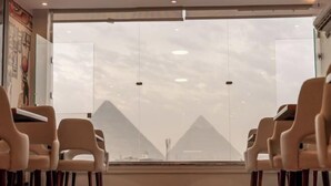 A room with a view of pyramids through large windows, a red carpet, and beige chairs. - The Muse Pyramids INN (Kafr Nassar)