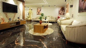 A modern living room with a marble floor, a flat-screen TV mounted on the wall, a beige sofa, a coffee table, and a decorative statue. - The Muse Pyramids INN (Kafr Nassar)