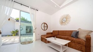 Ein modernes Wohnzimmer mit einem braunen Sofa, einem weißen Couchtisch und einem großen Fenster mit Vorhängen.