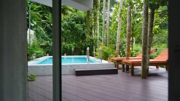 Un área de piscina con jacuzzi, terraza de madera y sillones de descanso.