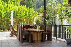 An outdoor wooden table and chairs on a patio with a view of tropical plants. - Tropical Oasis Aoyon Beach House (Phuket)