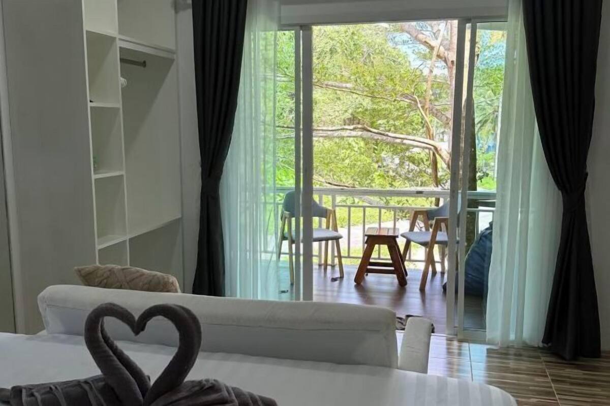A bedroom with a bed, a heart-shaped decoration on the bed, a wardrobe, and a balcony with chairs and a table.