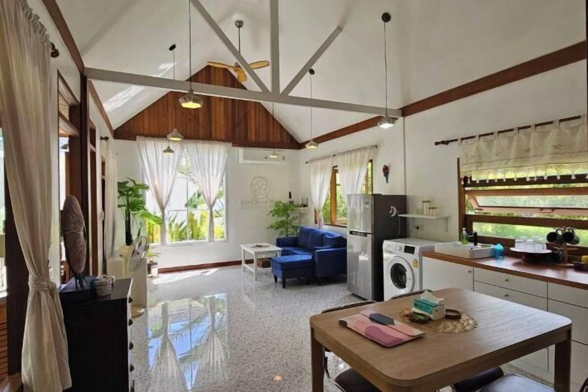 A room with a dining table, a sofa, a washing machine, and a ceiling fan.