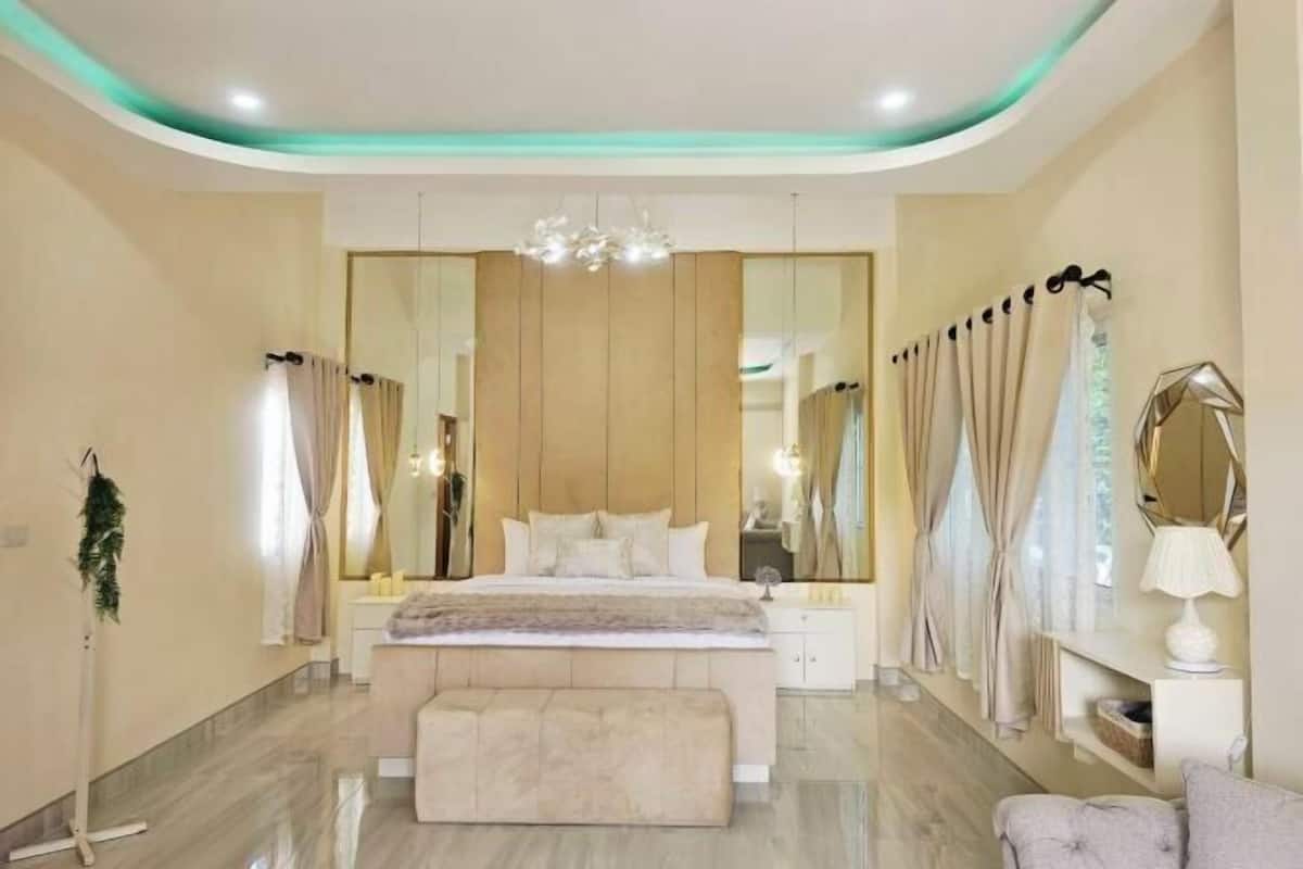 A modern bedroom with a large bed, a mirror, a chandelier, and a bench.