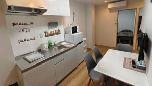 A compact kitchen with a microwave, sink, and a dining area with chairs. - Isshuku Ryokan Kotobuki Sanchome (Tokyo)