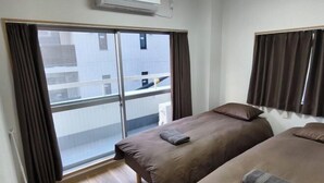A hotel room with two beds, a sliding glass door to a balcony, and an air conditioning unit on the wall. - Isshuku Ryokan Kotobuki Sanchome (Tokyo)