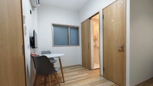 A small room with a wooden floor, a white table with two chairs, a window with blinds, and a door leading to another room. - Isshuku Ryokan Kotobuki Sanchome (Tokyo)