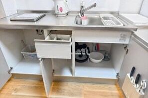 Una cocina con un lavamanos, una tetera, una cafetera, una balanza y un bloque de cuchillos.