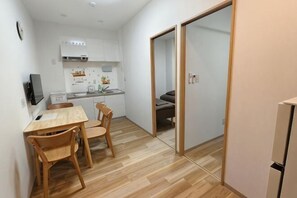 A compact kitchen with white cabinets, a wooden dining table, and chairs. - Isshuku Ryokan Kotobuki Sanchome (Tokyo)