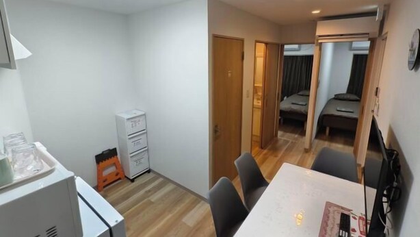 A compact hotel room with a wooden floor, a dining table with chairs, a small kitchenette, and a separate sleeping area with a bed. - Isshuku Ryokan Kotobuki Sanchome (Tokyo)
