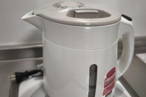 A white electric kettle with a handle and a lid, placed on a surface. - Isshuku Ryokan Kotobuki Sanchome (Tokyo)