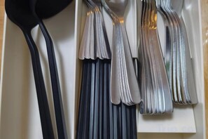 Une collection de divers ustensiles de cuisine, notamment des cuillères, des fourchettes et des couteaux, disposés sur une étagère.