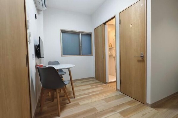 A compact room with a dining table and chairs, a window, and a sliding door leading to a bathroom. - Isshuku Ryokan Kotobuki Sanchome (Tokyo)