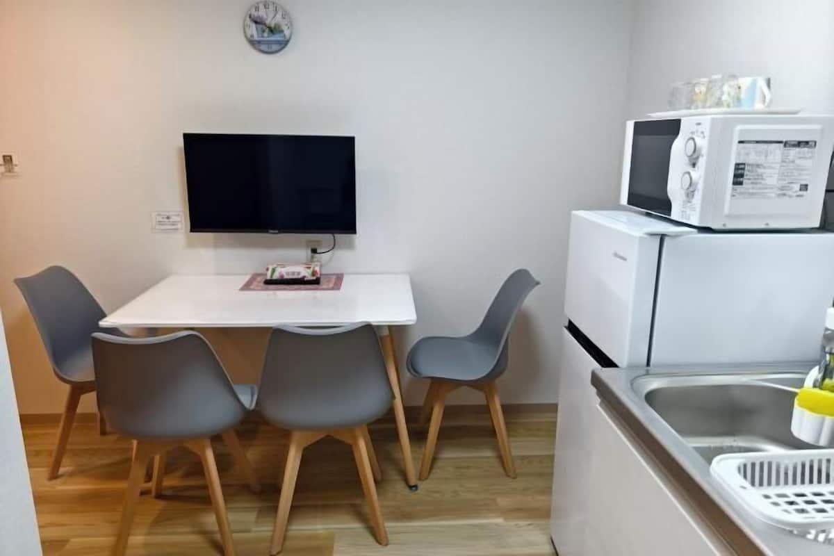 Eine kleine Küche mit einem weißen Tisch, vier grauen Stühlen, einer Mikrowelle, einem Kühlschrank und einem Spülbecken.