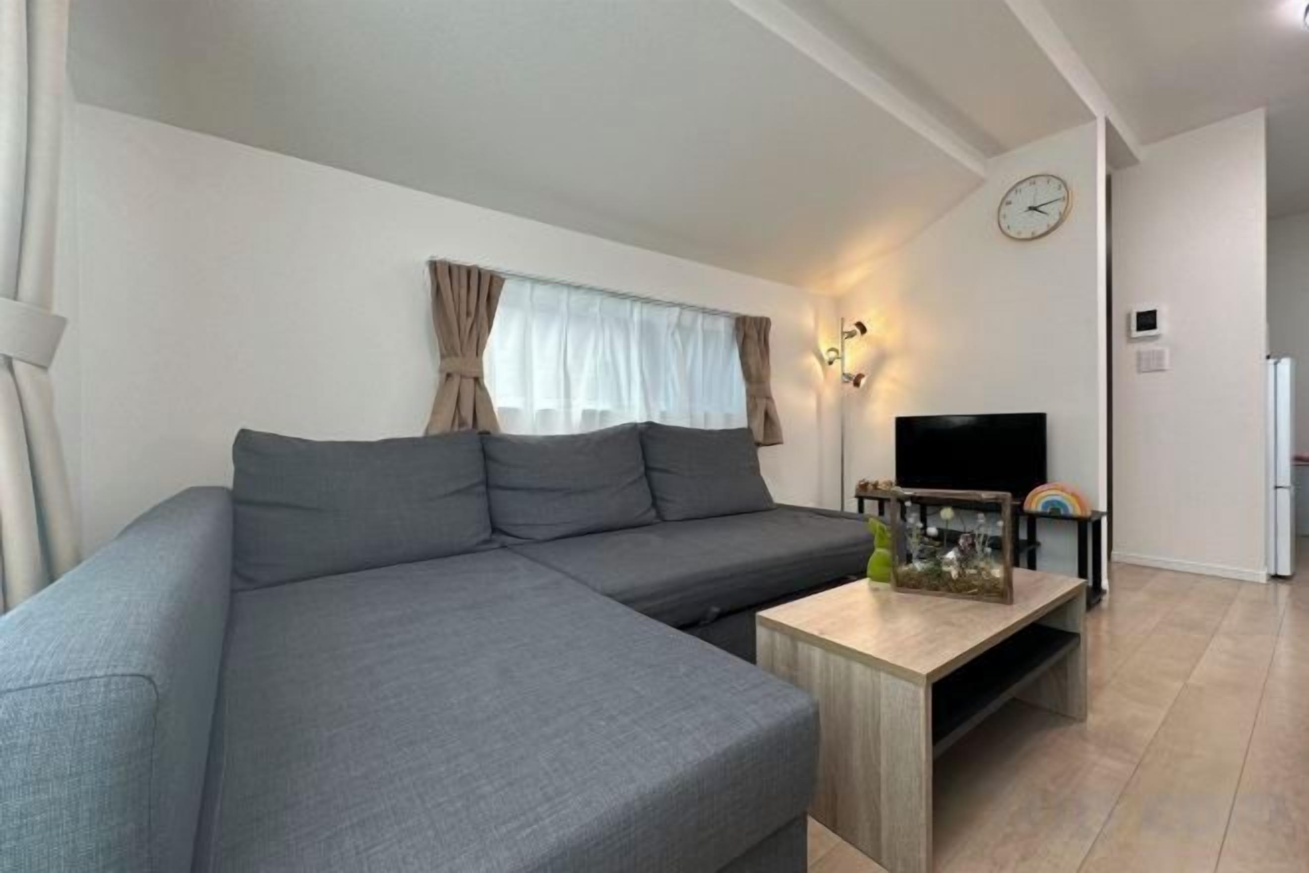 A living room with a sofa, a coffee table, a flat-screen TV, and a clock on the wall.