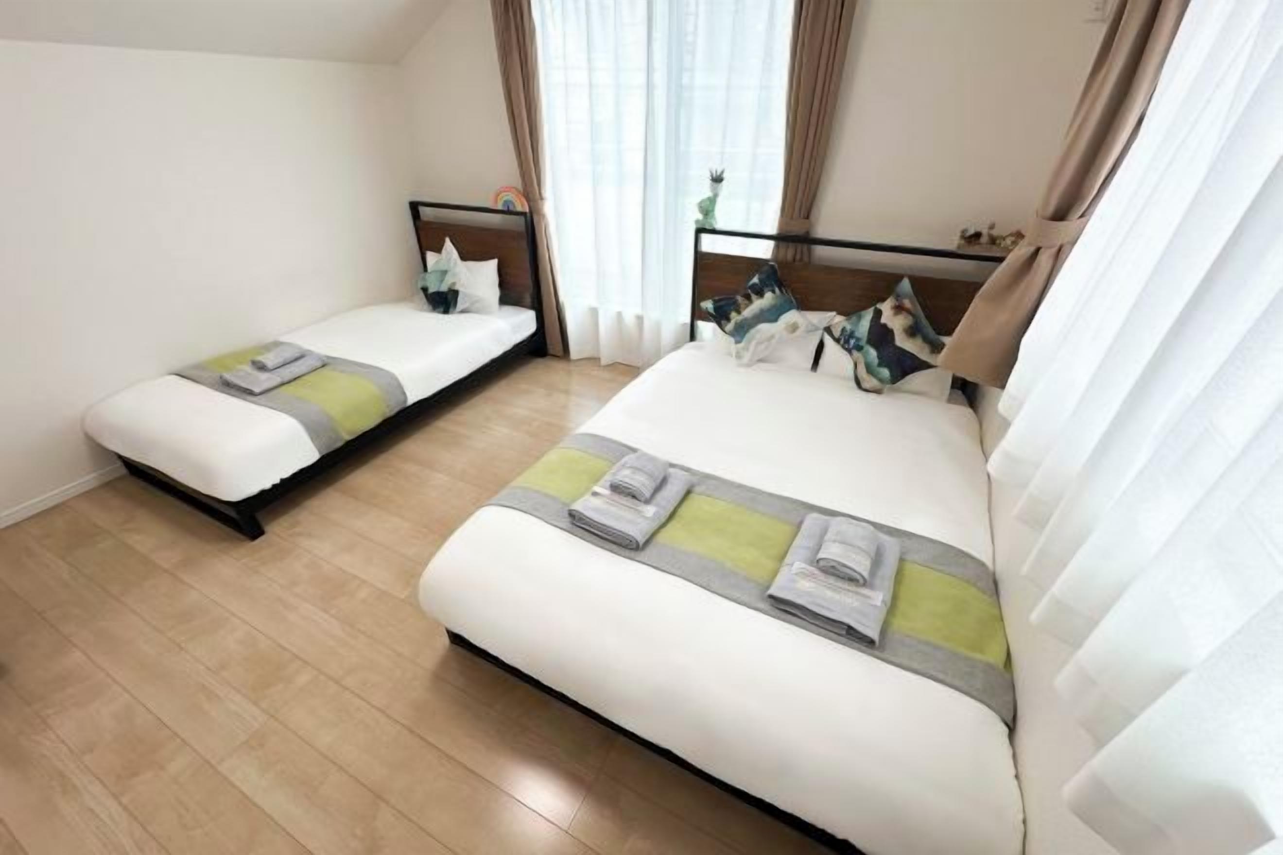 Een hotelkamer met twee bedden, een houten vloer en een raam met gordijnen.