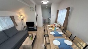 A modern living room with a sofa, a dining table set for four, and a kitchen in the background. - nestay villa tokyo itabashi (Tokyo)