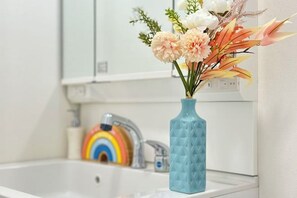 A bathroom with a white sink, a blue vase with flowers, and a rainbow-colored faucet. - nestay villa tokyo itabashi (Tokyo)