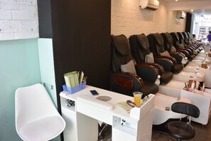 A row of massage chairs with footrests, a white counter with a phone, and a small trash bin. - The Hotel Nicecy (Ho Chi Minh City)
