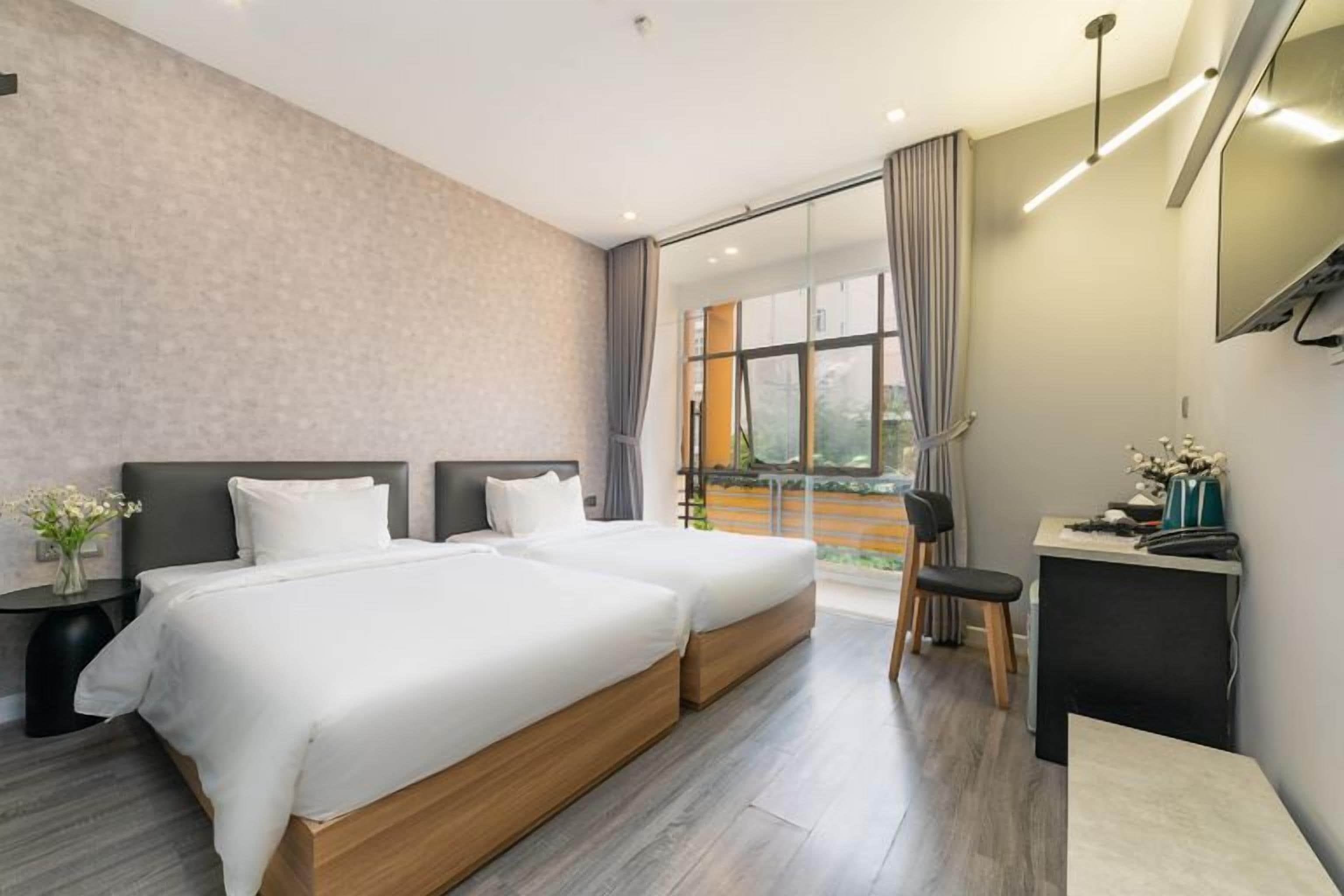 Habitación de hotel con dos camas, un escritorio, una silla y un ventanal con cortinas.