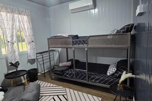 A bunk bed room with a small table and a chair, a window with curtains, and an air conditioning unit. - The Vanilla Cabin 2 (Kuala Terengganu)