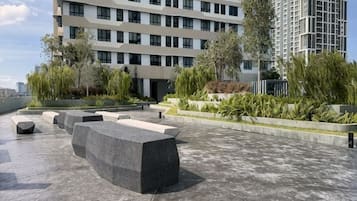 A rooftop terrace with seating areas, greenery, and modern buildings in the background.