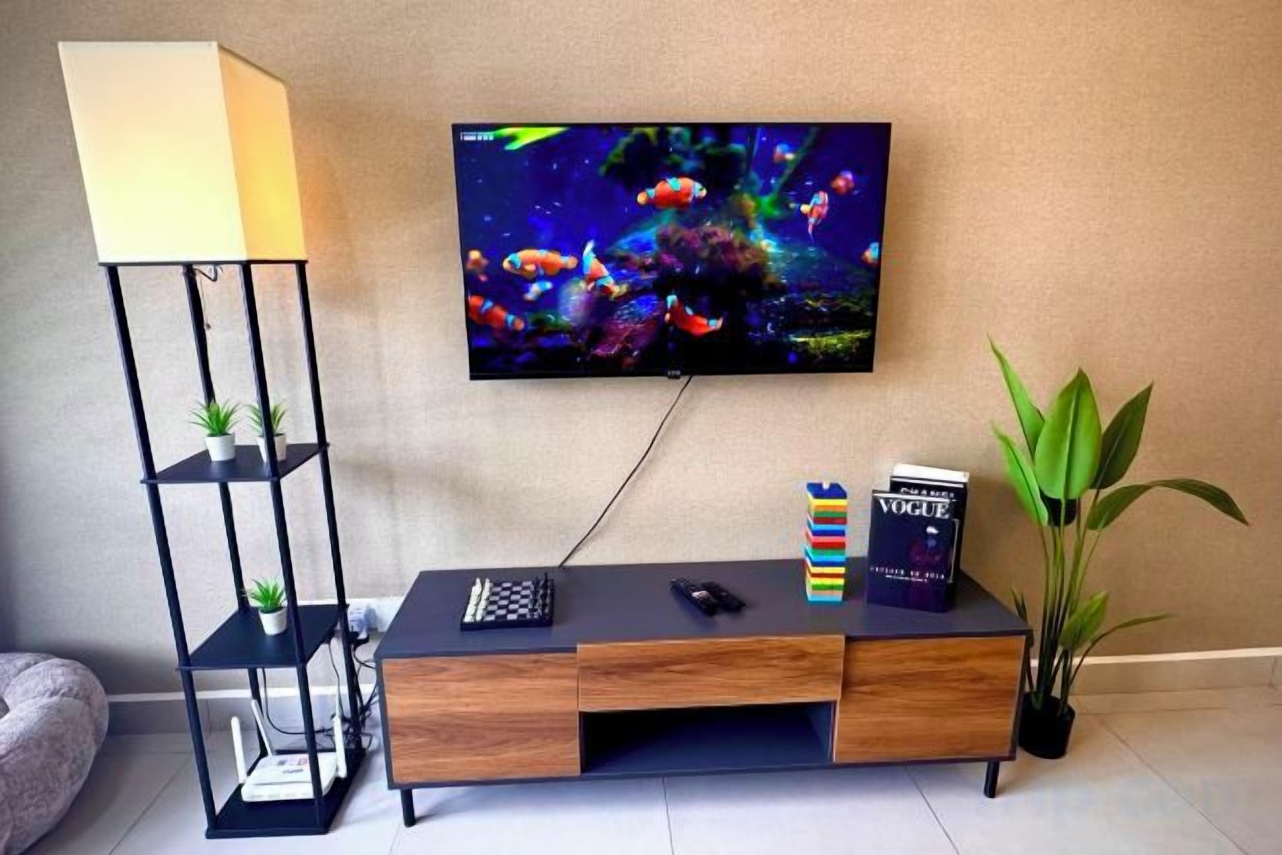 A living room with a TV, a black entertainment unit, a lamp, and a plant.