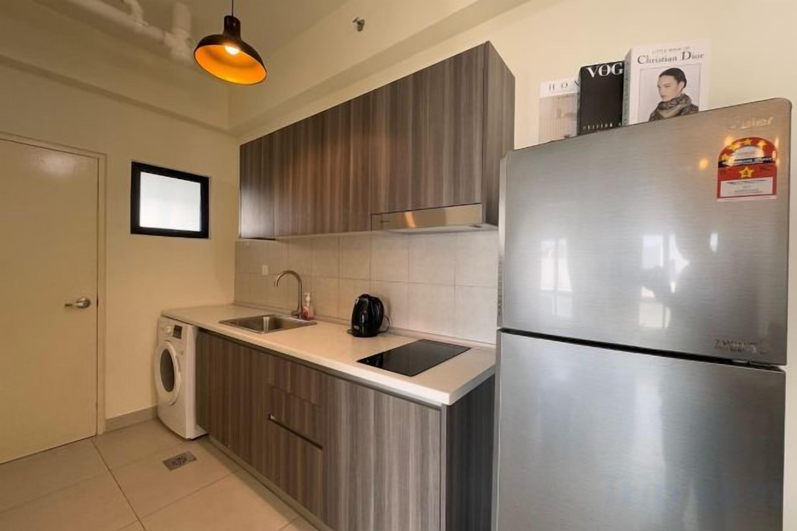 A compact kitchen with a stainless steel refrigerator, a washing machine, and a sink.