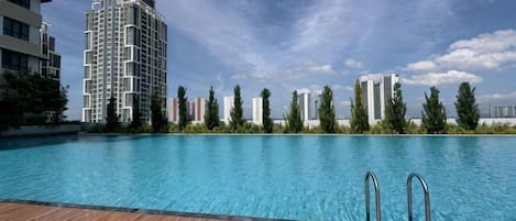 A swimming pool with wooden deck, surrounded by modern buildings and trees.
