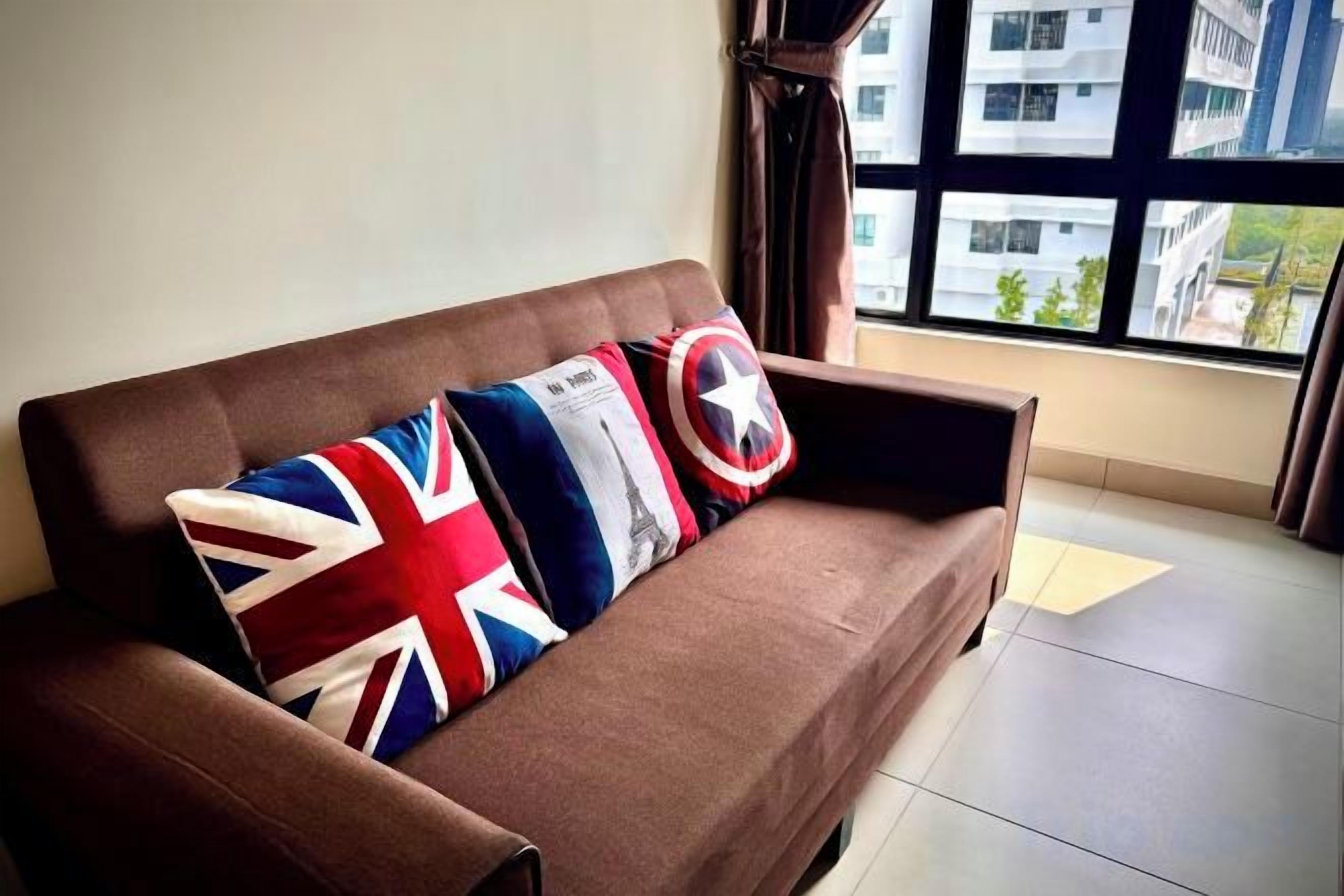 Un sofá marrón con tres almohadones, uno con estampado de la bandera del Reino Unido, otro con diseño rojo y blanco, y un tercero con patrón blanco y rojo.