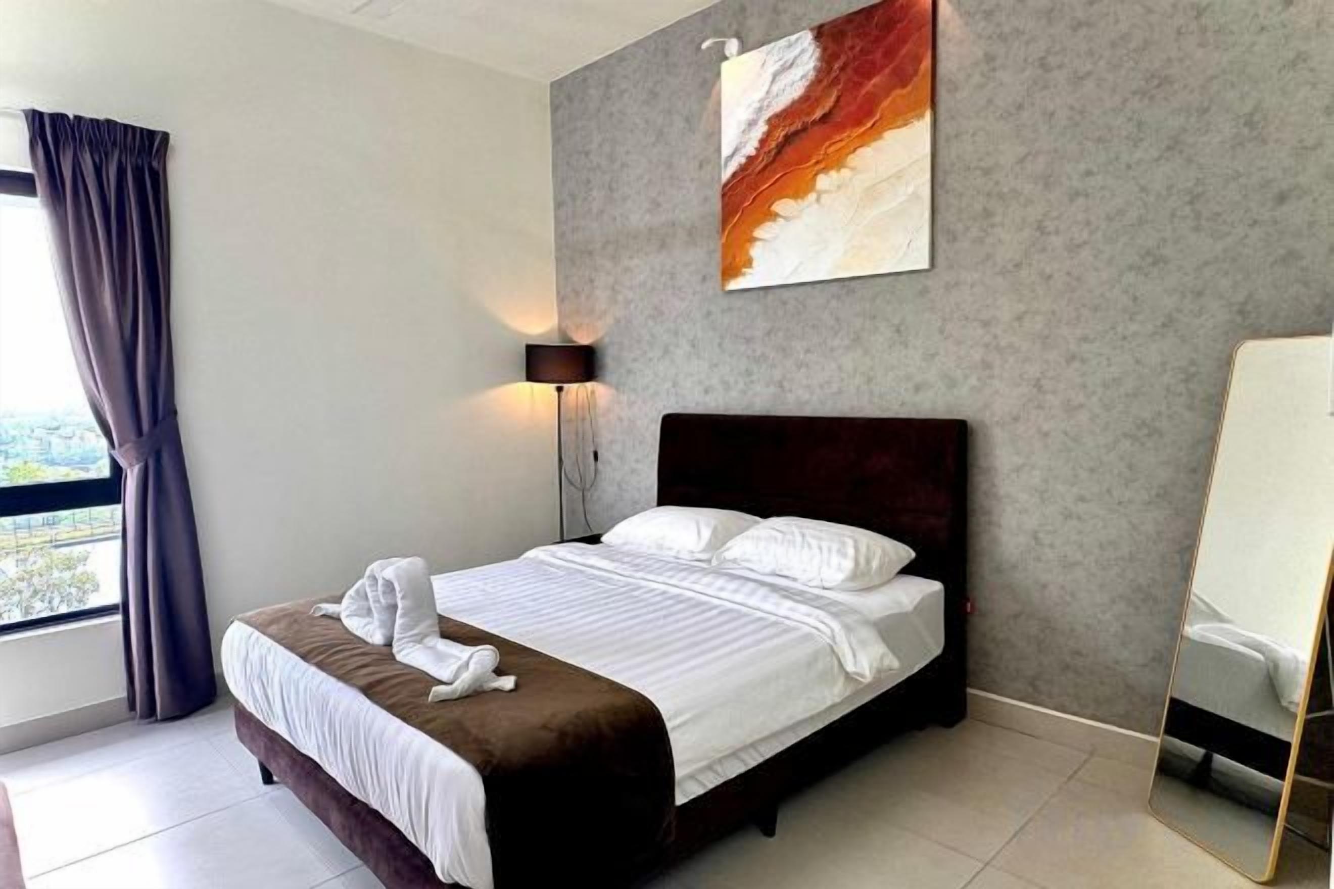 A hotel room with a bed, a bedside table, a lamp, a window with curtains, and a painting on the wall.