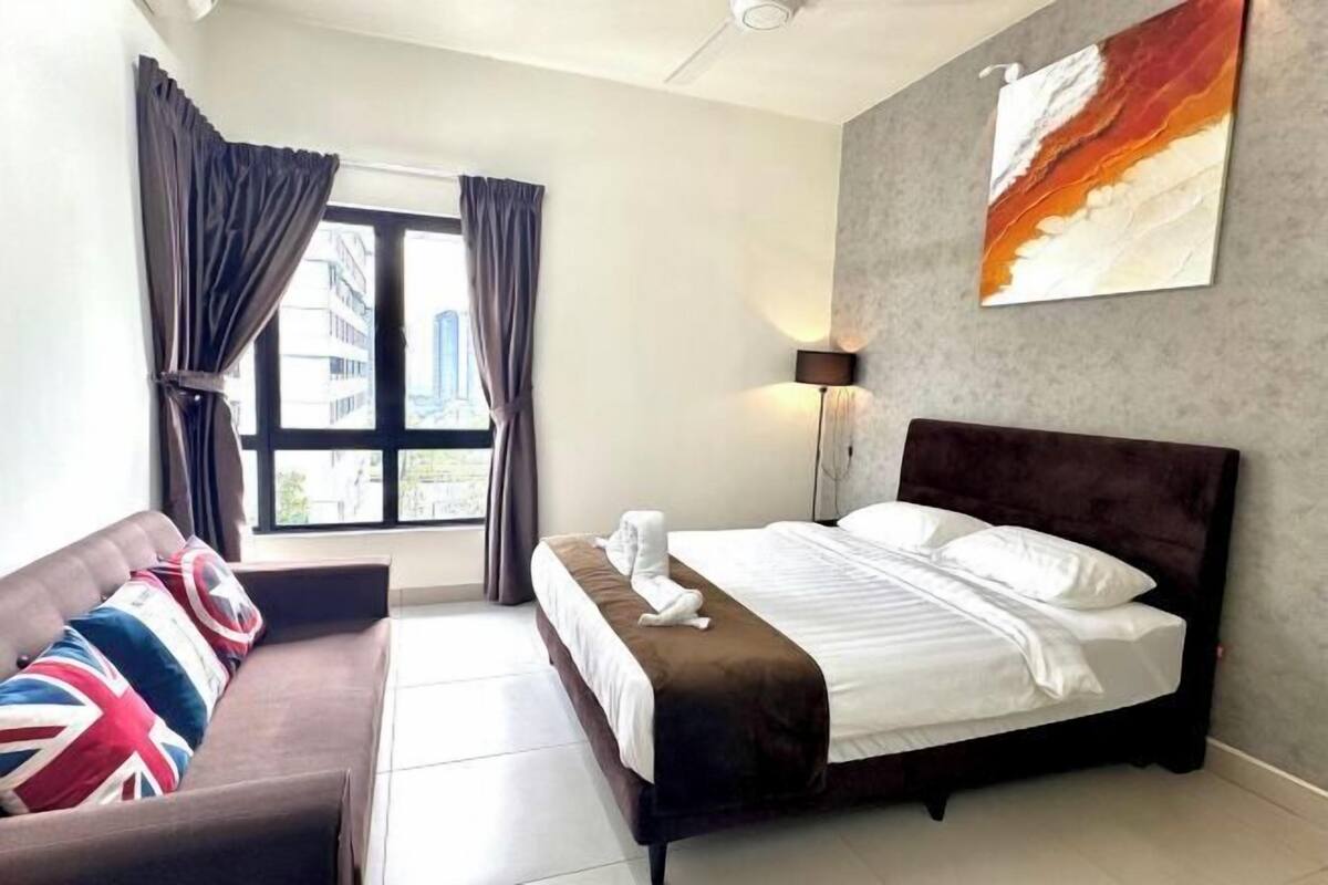 A hotel room with a bed, a sofa, a window with curtains, a lamp, and a painting on the wall.