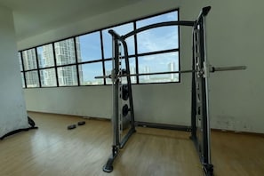 A gym with a squat rack, a bench press, and a barbell. There are windows with a view of buildings outside. - 2R2B Sweet Home Cyberjaya Suites (Cyberjaya)