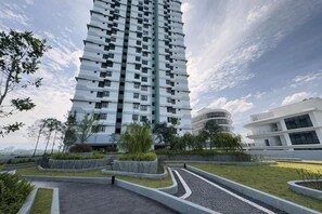 Een modern hoog gebouw met een gebogen vorm, omringd door aangelegde gebieden met paden en groen.