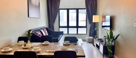 A modern living room with a dining area, a sofa, and a TV on the wall.