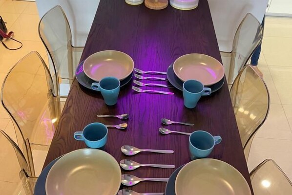 A dining table with blue cups, spoons, and plates arranged for a meal.