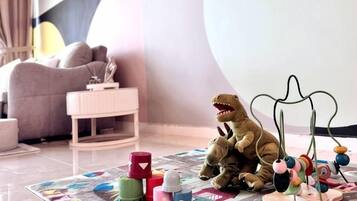 A dinosaur toy on a play mat with a hanging toy in a room with a sofa and a small white table.