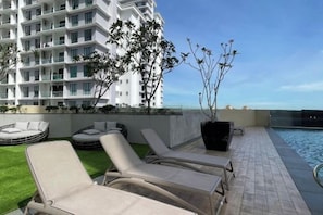 A rooftop pool area with lounge chairs, a small pool, and a view of a high-rise building. - L22-ParadigmMall Residence Skudai JB 3R2B-10pax by UcomeHomestay (Tebrau)