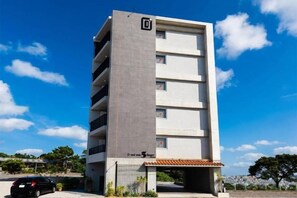 A multi-story building with a parking area in front. - D-and Stay. 5 Resort Okinawa (Urasoe)