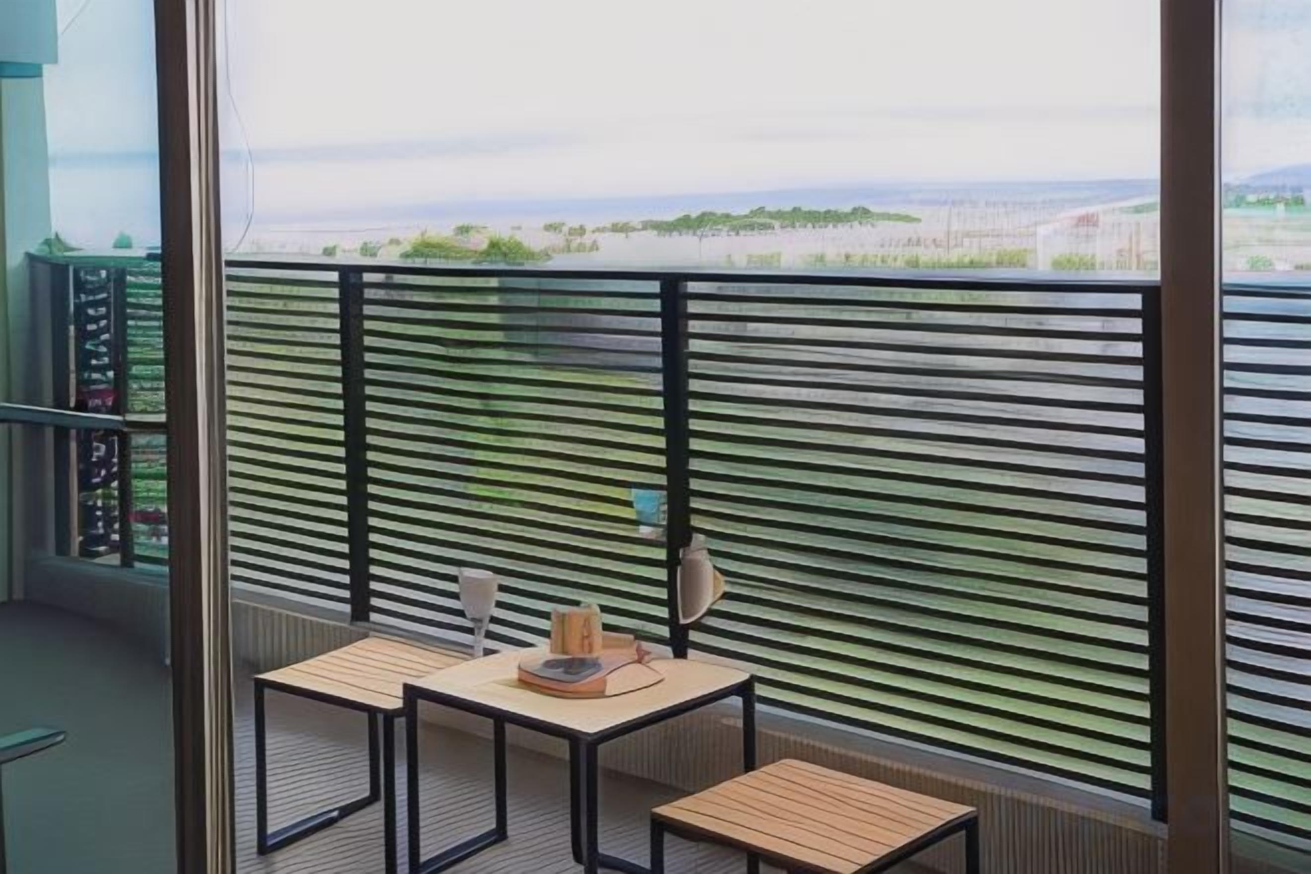 A balcony with a view of a green landscape, two tables with chairs, and a railing.
